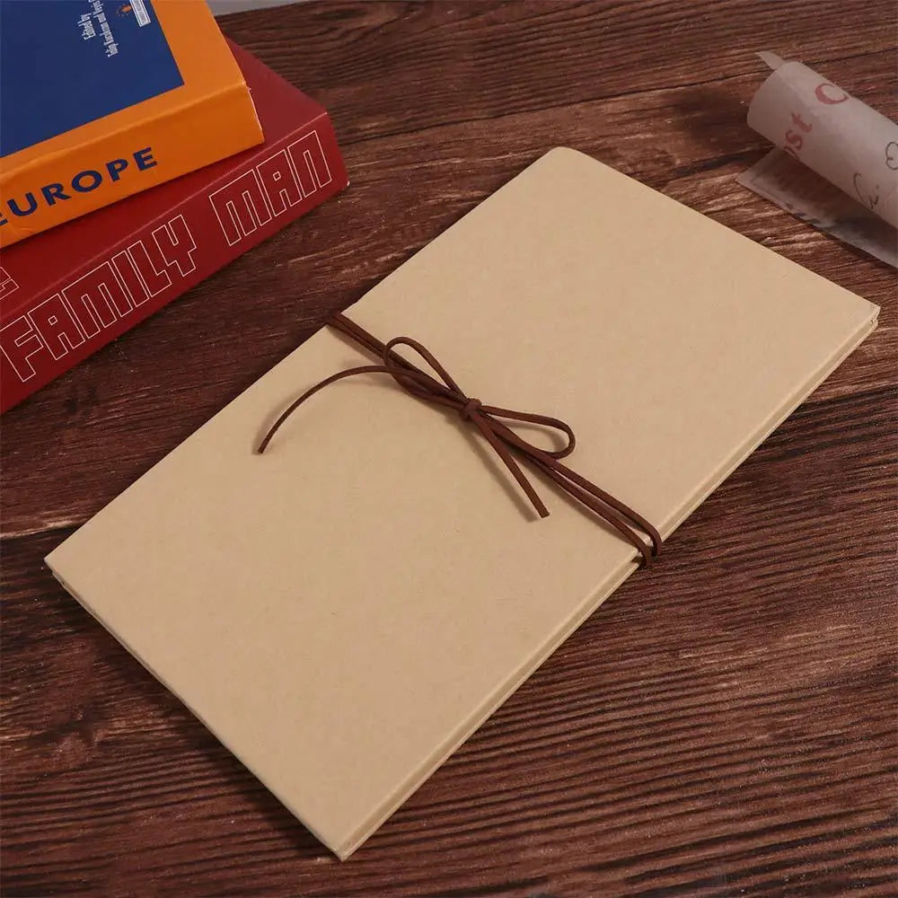 A light beige accordion photo album lying on a wooden surface with a brown leather tie.