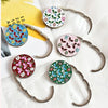 A collection of floral crystal handbag hooks with silver-toned metal arms and colorful round crystal accents.