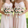 Two brides in pink gowns hold bouquets of light pink roses and greenery