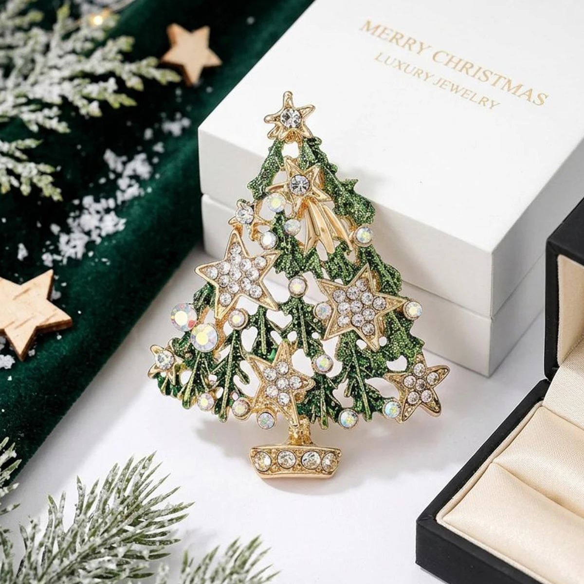 A gold-toned rhinestone Christmas tree brooch pin displayed on a white box with green velvet and pine branches.
