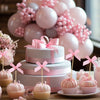 A tiered pink cake display featuring pink bow cupcake toppers and pink balloons for a celebration.