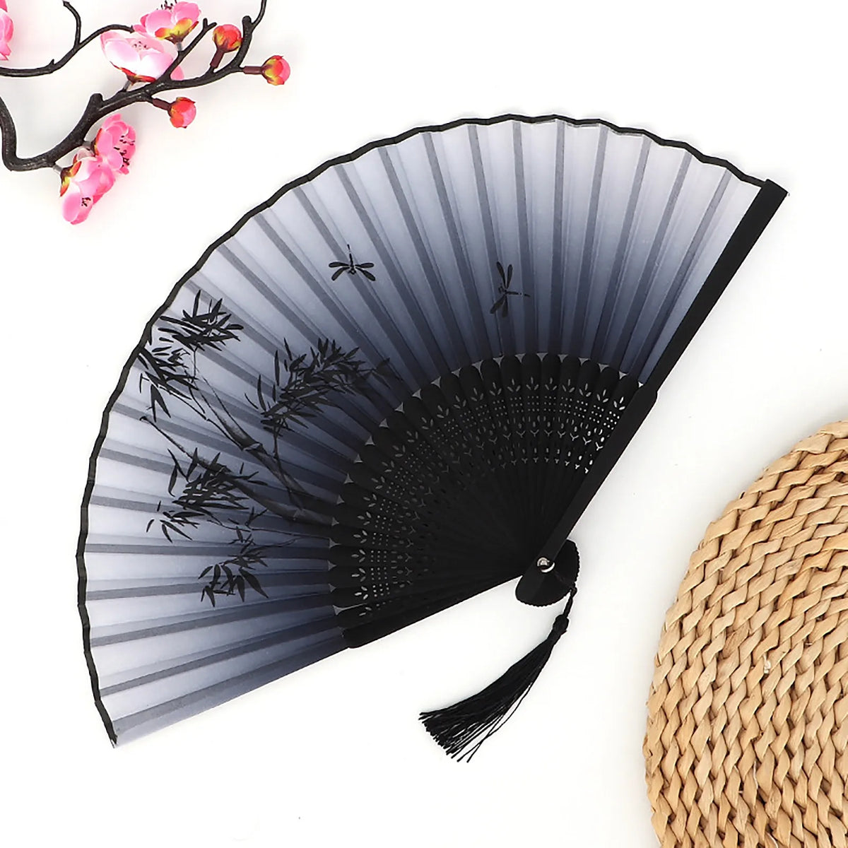 A black and gray vintage bamboo folding fan with a scalloped edge is shown next to a woven straw fan.