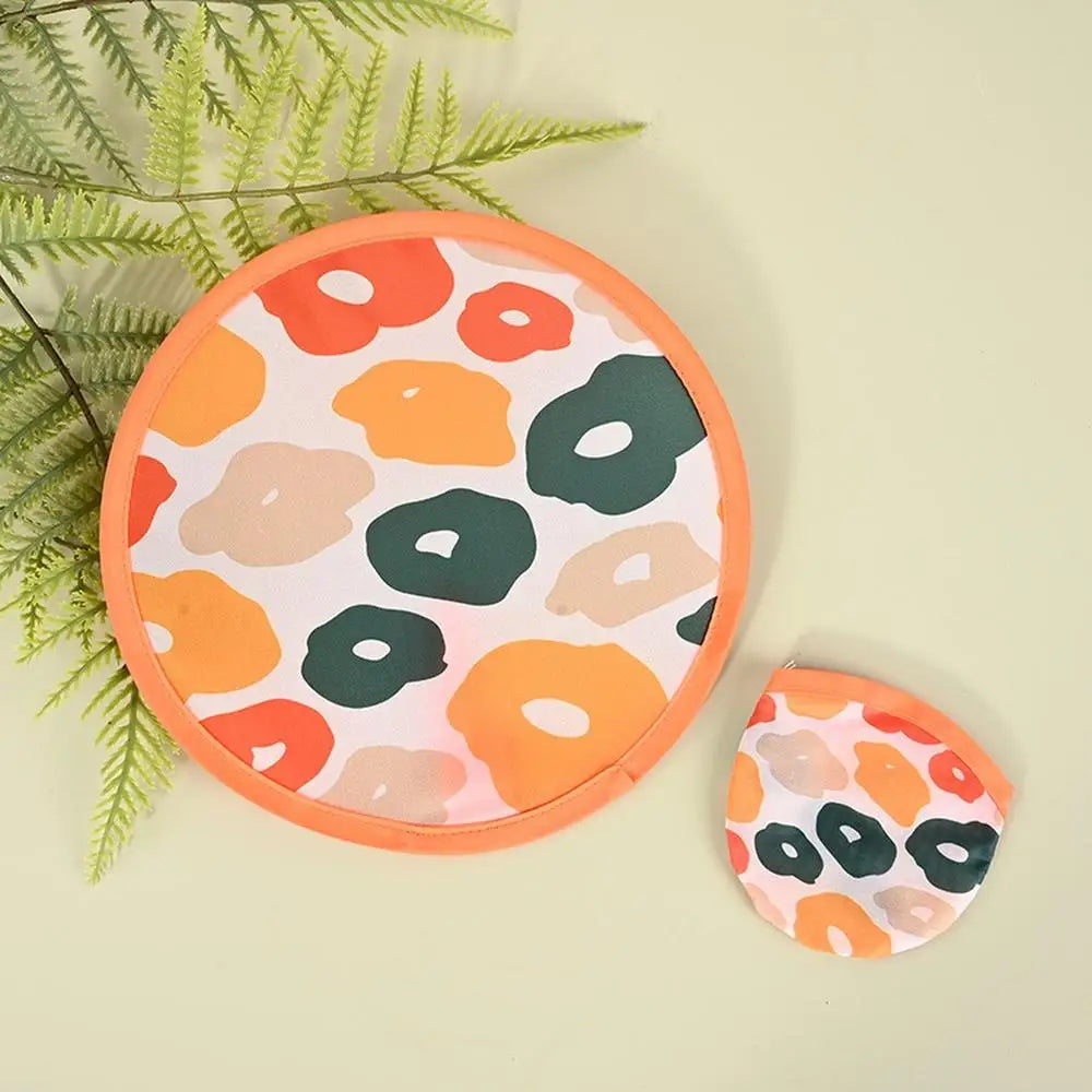 A round silicone cooling fan with an orange and green abstract floral pattern resting on a light green surface.