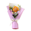 A bouquet of handcrafted crochet flowers featuring an orange sunflower and purple daisies wrapped in pink paper.