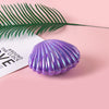 A purple seashell shaped item is placed next to a green palm frond on a pink background.