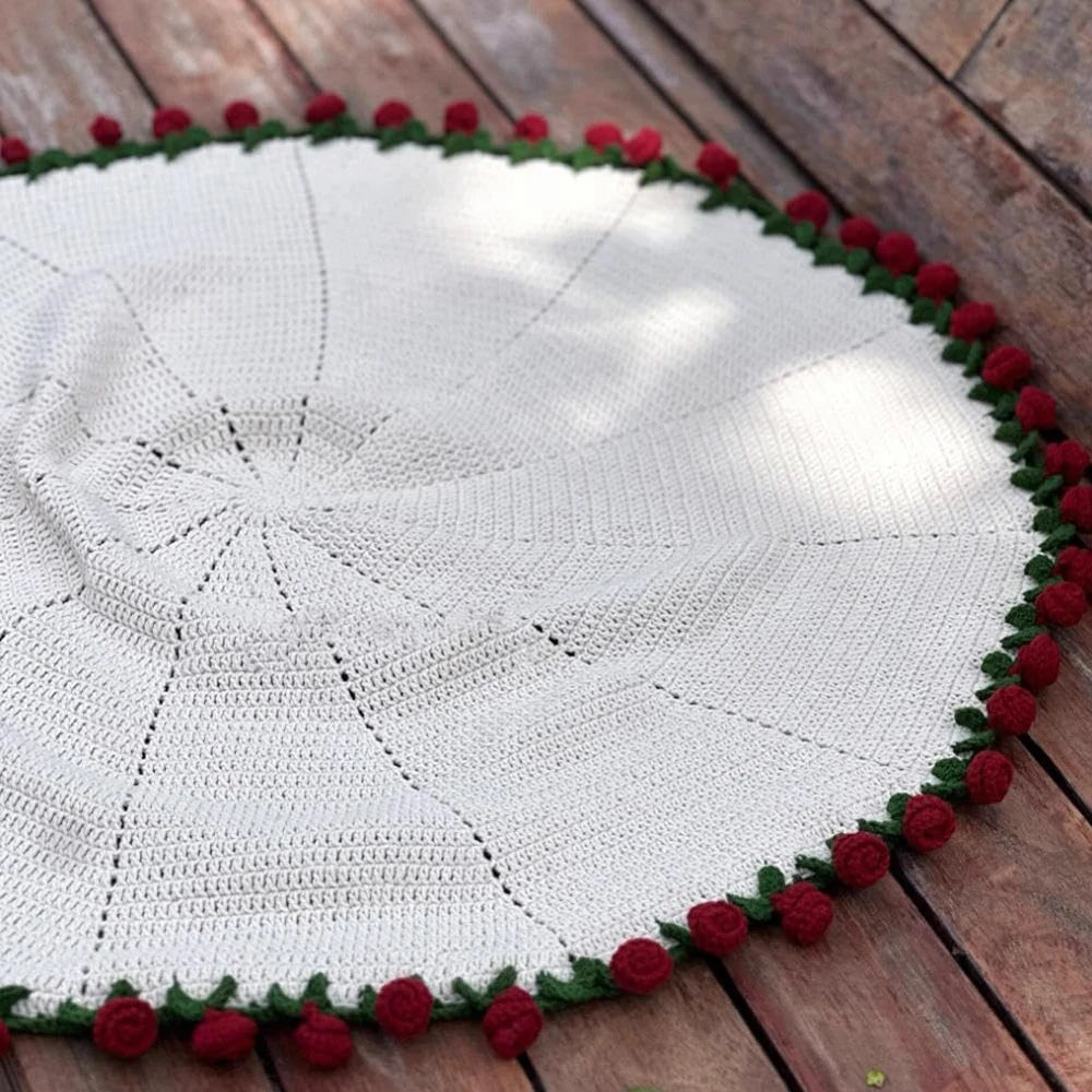 Handmade rose bouquet blanket gift featuring a cream-colored knitted blanket with a red floral border on a wooden surface.