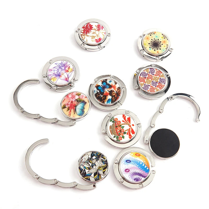 A collection of foldable handbag hooks featuring various floral and geometric designs in silver metal.