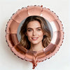 A person's face is framed within a large, rose gold foil balloon shaped like a wreath.