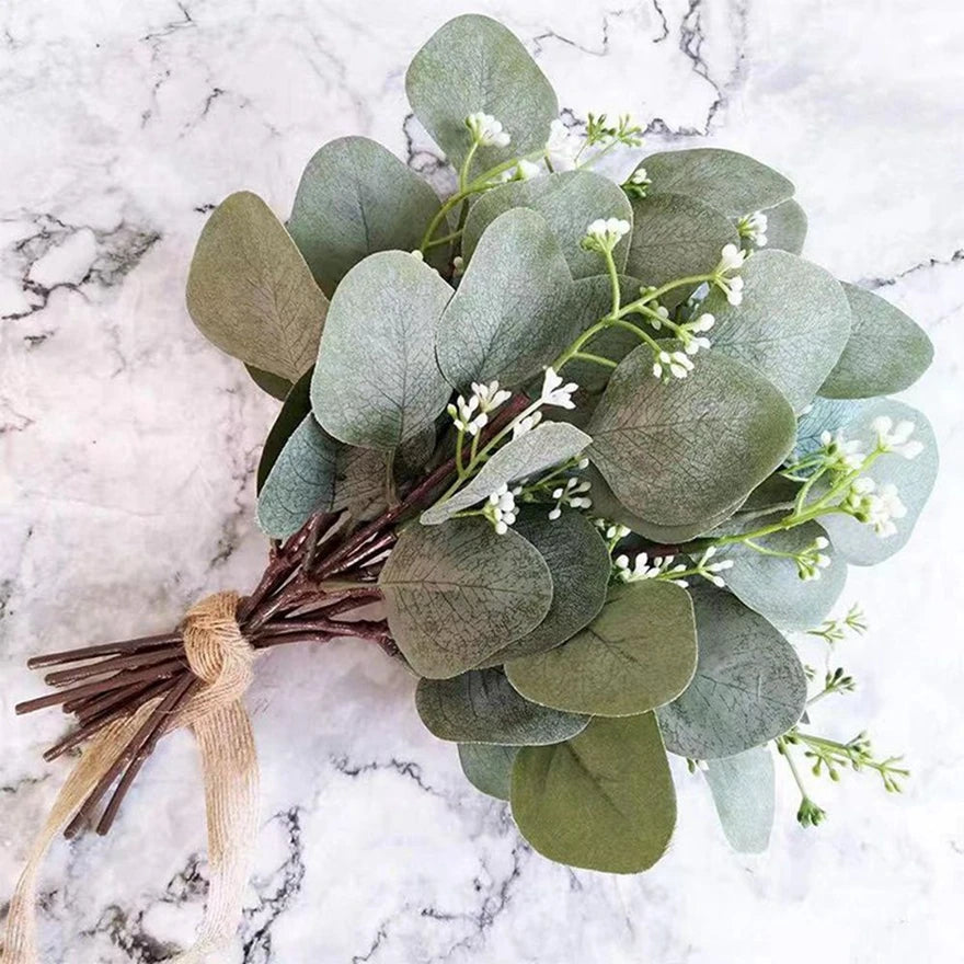 A bundle of artificial eucalyptus stems with silvery-green leaves and small white flowers on a light marble surface.