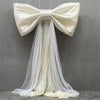 A large white satin bow with a long sheer tulle drape displayed against a gray background.