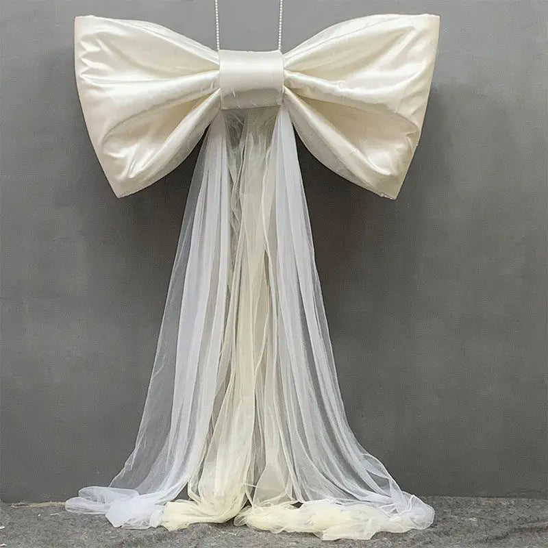 A large white satin bow with a long sheer tulle drape displayed against a gray background.