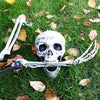 A realistic white skeleton hand lawn stake lying on green grass amidst fallen autumn leaves.