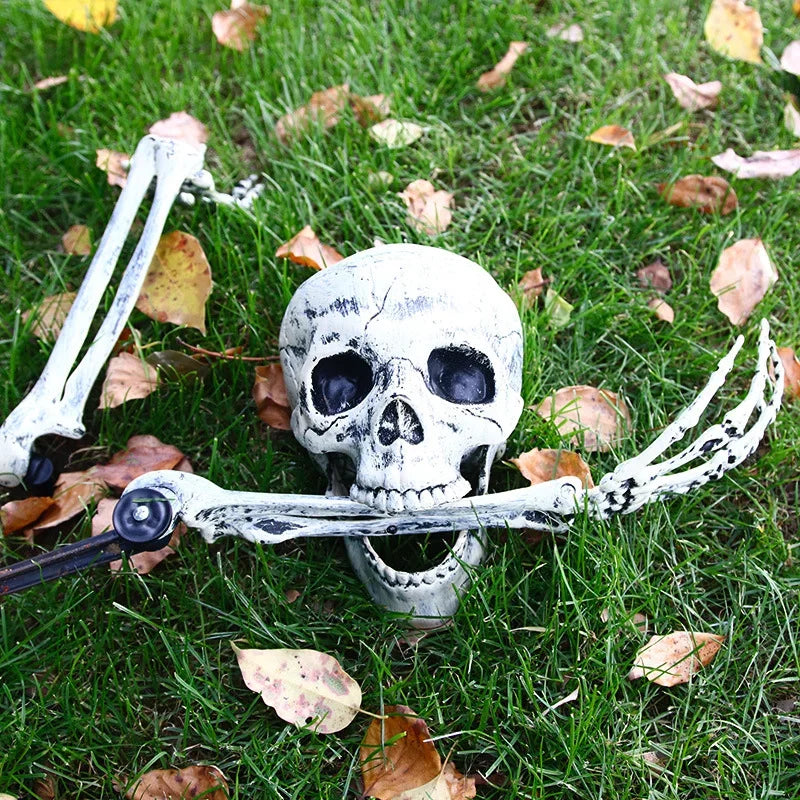 A realistic white skeleton hand lawn stake lying on green grass amidst fallen autumn leaves.