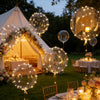 A golden-lit outdoor wedding or party scene featuring numerous illuminated balloons and tables.