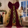 A woman stands beside an elegant velvet Christmas tree decorated with lights and ornaments.