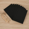 A stack of black photo frames and a rustic wooden clip display are arranged on a light wood surface.