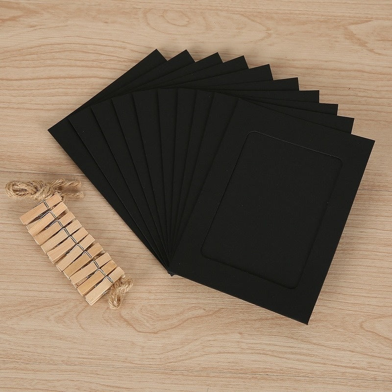 A stack of black photo frames and a rustic wooden clip display are arranged on a light wood surface.