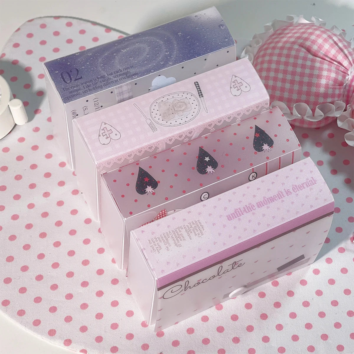 Tres cajas de almacenamiento minimalistas rosas con tapas decorativas y pegatinas, exhibidas sobre una superficie de lunares 
