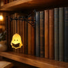 A vintage bookshelf lantern lamp with a yellow glow illuminates a row of old books on a wooden shelf.