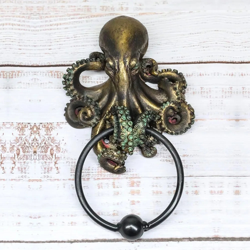 A bronze octopus skull door knocker featuring a cast iron ring, displayed on a white wooden surface.