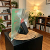 A minimalist black display stand holding a clear vinyl record and CD, set on a woven natural fiber base.