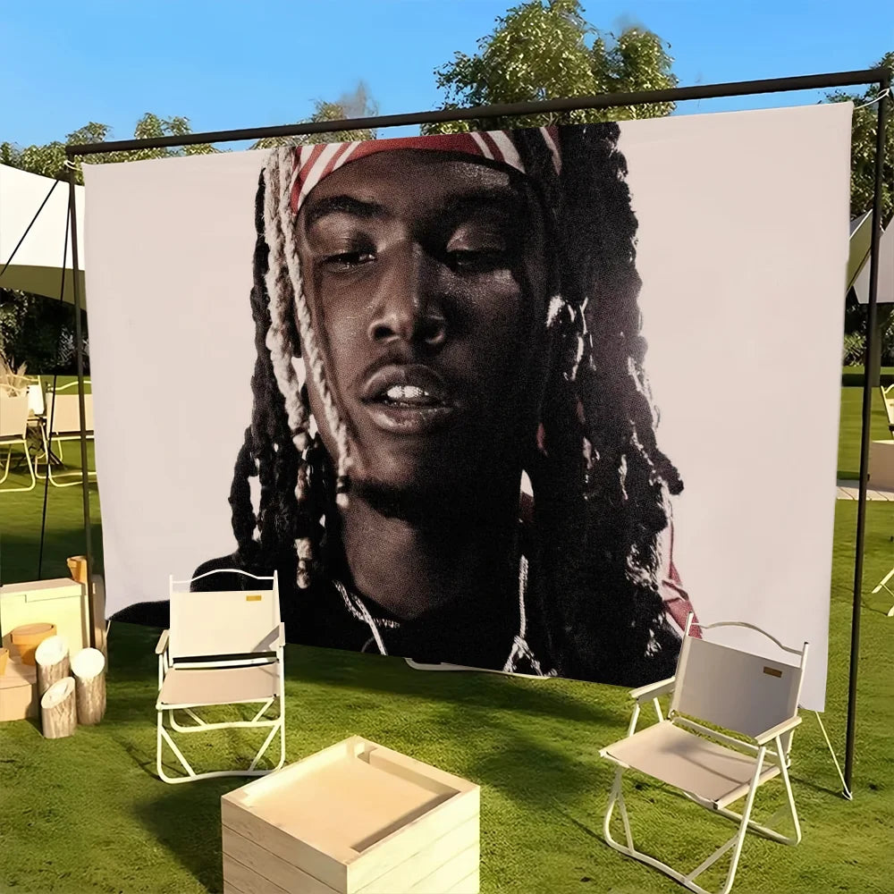 A portrait of a man with dreadlocks and a bandana displayed on a large white wall tapestry outdoors.