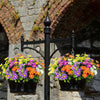 A black wrought iron bracket holds two potted bouquets of colorful silk daisies against a stone wall.