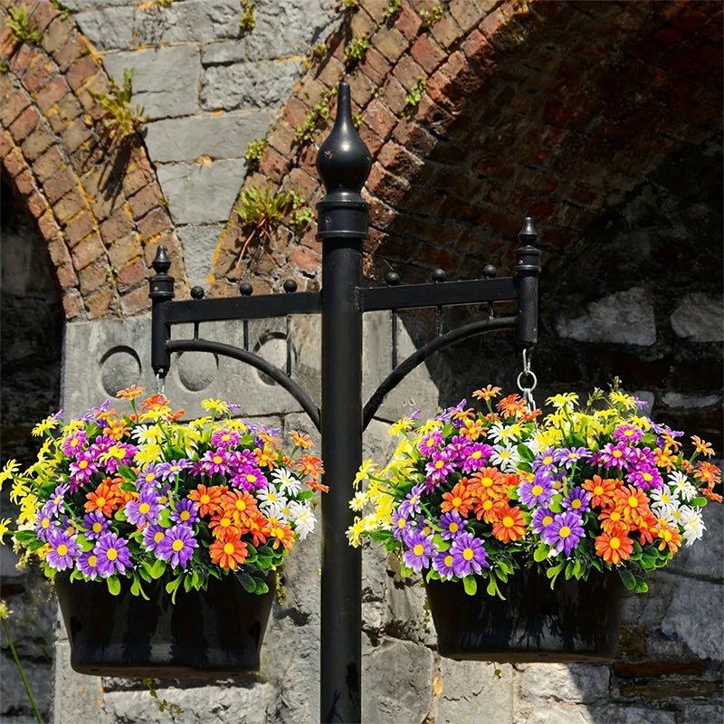 A black wrought iron bracket holds two potted bouquets of colorful silk daisies against a stone wall.