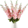 Un bouquet de fleurs artificielles de delphinium roses et blanches dans un vase blanc.
