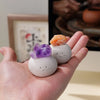 A hand holds a white bean-shaped decorative stone and an orange crystal on a light background.