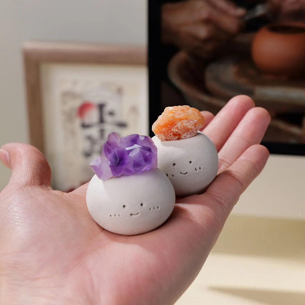 A hand holds a white bean-shaped decorative stone and an orange crystal on a light background.