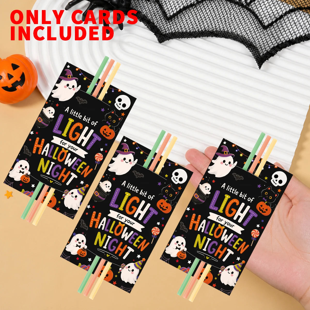 A hand holds several Halloween glow stick holder cards with festive designs and wooden sticks.