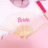 A pink hand fan with the word Bride written on it, displayed on a pink background.