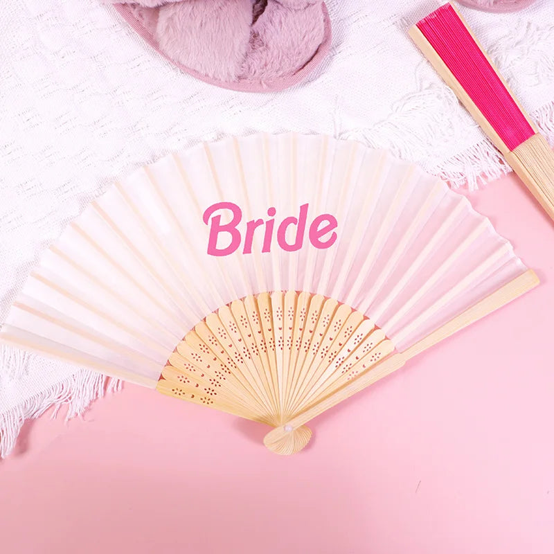 A pink hand fan with the word Bride written on it, displayed on a pink background.