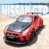 A red Nissan GT-R sports car model is displayed on a sandy surface with water in the background.