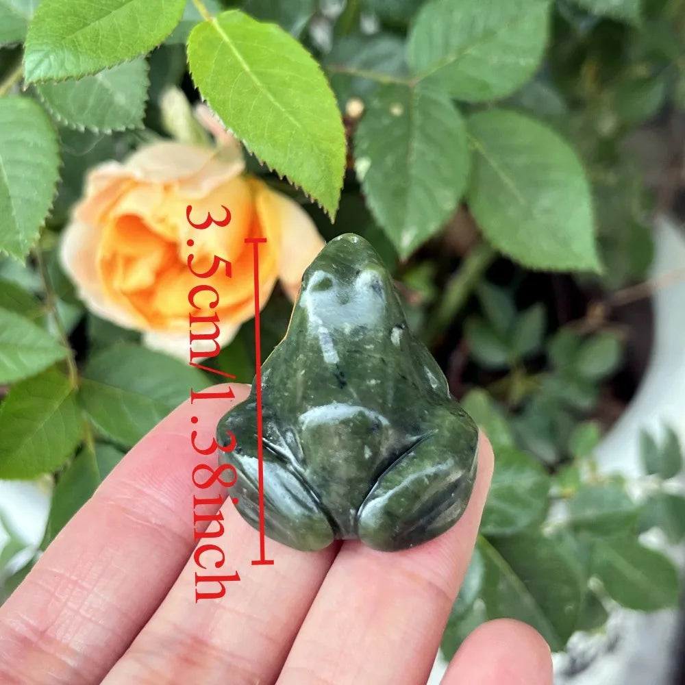 Une petite figurine de grenouille de jade verte est tenue dans une main, avec une échelle indiquant sa taille de 3,5 cm.