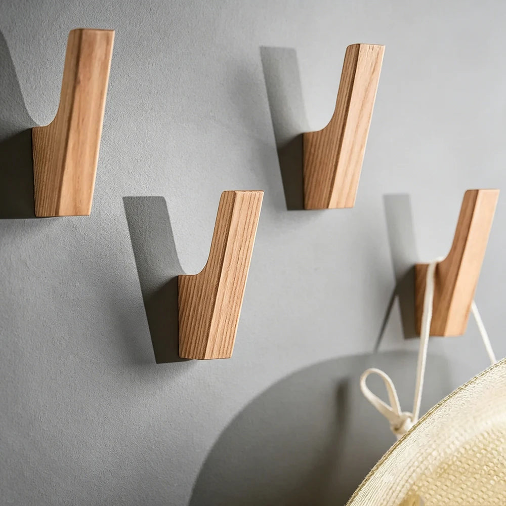 Drei natürliche Holz-Wandhaken unterschiedlicher Größe an einer grauen Wand montiert.