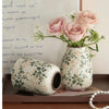 A handmade ice crackle ceramic vase filled with pink roses and greenery on a wooden surface.