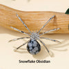 Silver crystal spider figurine with a black and white snowflake obsidian body resting on a wooden surface.