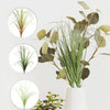 A bundle of artificial grass greenery with long green blades and large, rounded leaves in a white vase.