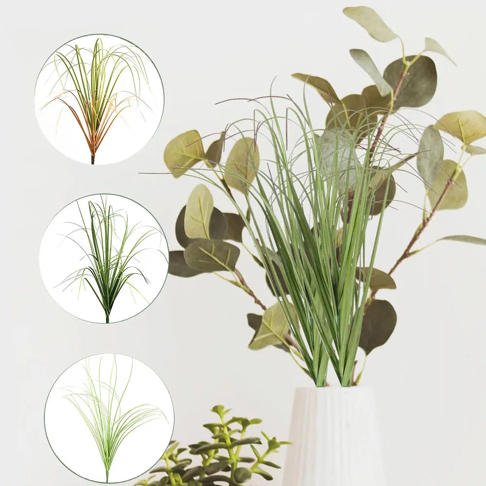 A bundle of artificial grass greenery with long green blades and large, rounded leaves in a white vase.