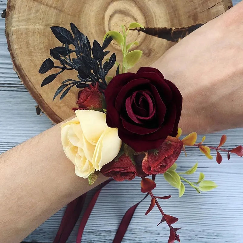 A hand holds a bouquet of deep red and cream velvet artificial roses with green foliage.