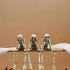 A set of realistic Halloween skeleton resin statues displayed on a white surface with autumn leaves.