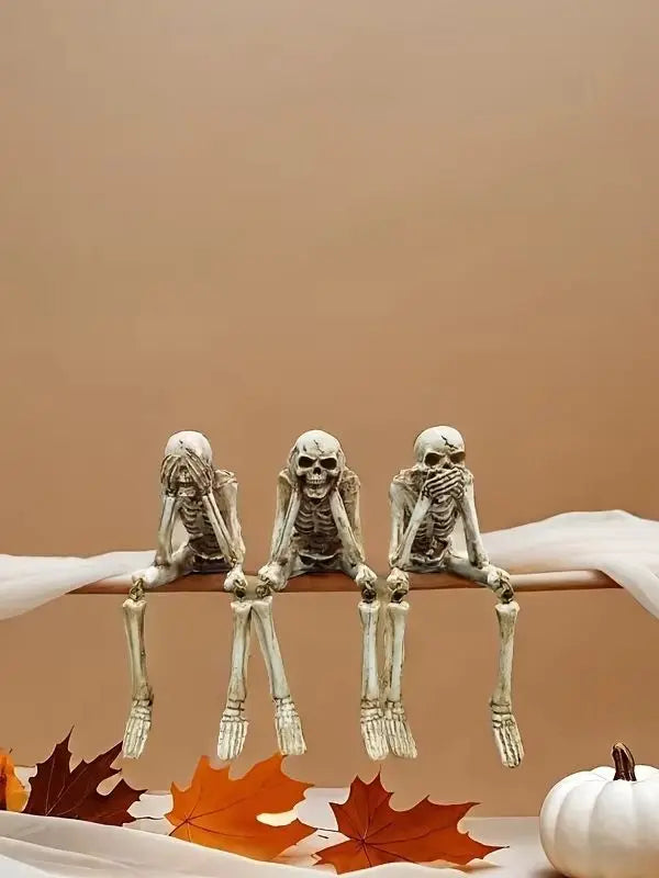 A set of realistic Halloween skeleton resin statues displayed on a white surface with autumn leaves.
