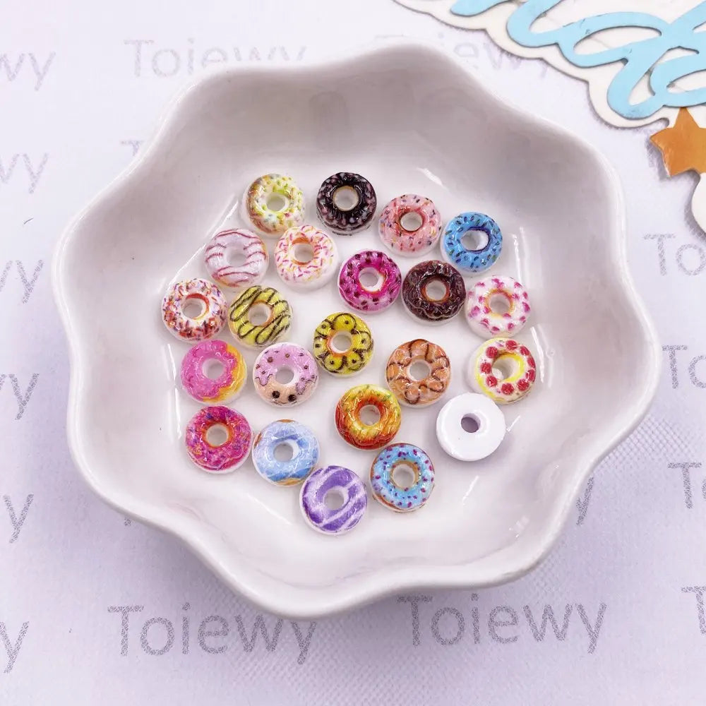 A white dish holds a mixed set of 60 resin cheese and donut nail art charms in various colors.
