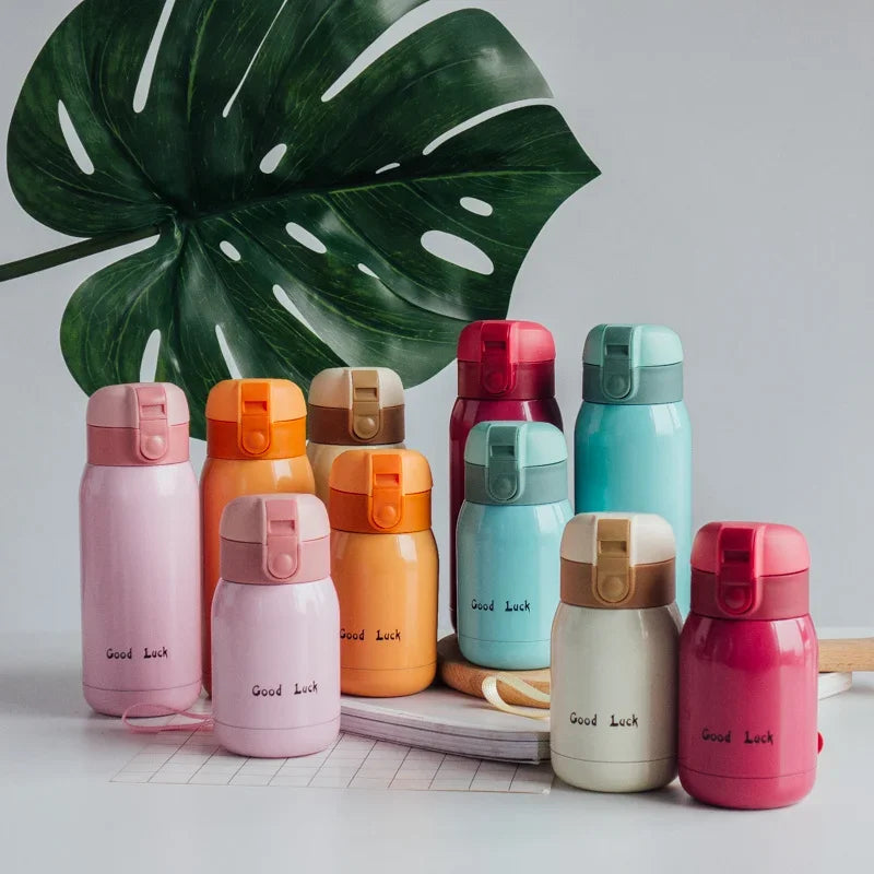 A collection of pink, orange, and mint green stainless steel vacuum insulated coffee mugs arranged in front of a large green 