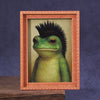 A framed picture of a green frog with black spiky hair inside a wooden frame.