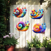 Three colorful metal snails in various spirals displayed on a white wooden background with greenery and potted plants.