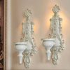 A pair of ornate white vintage wrought iron wall-mounted candle holders with decorative foliage.