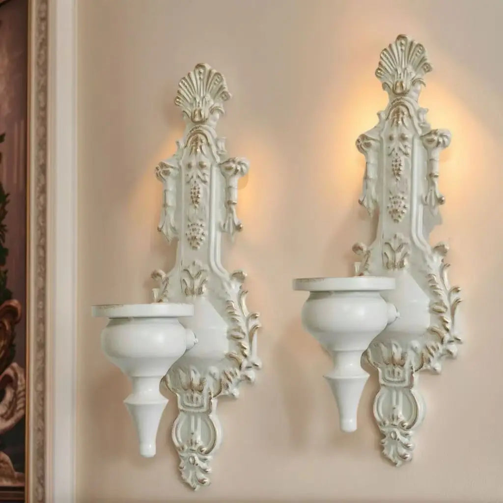 A pair of ornate white vintage wrought iron wall-mounted candle holders with decorative foliage.